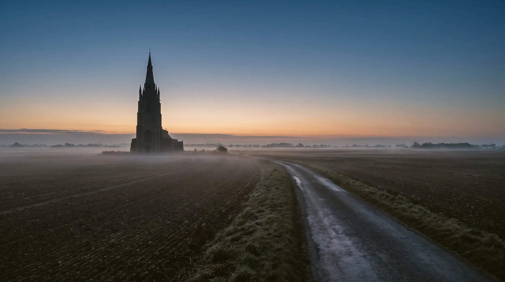 The tower of a fenland church rising over misty fields at dawn near Boston