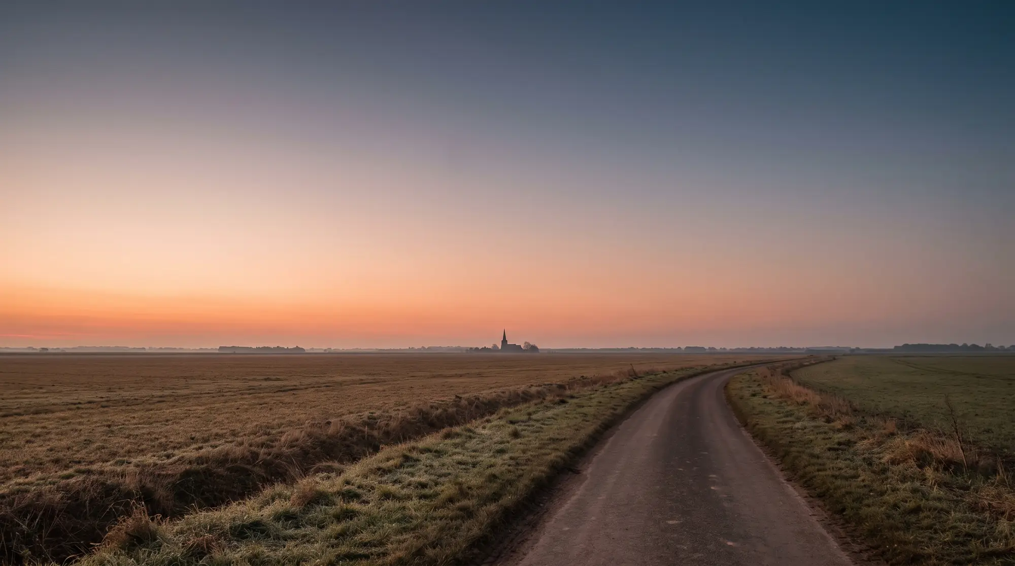 A quiet lane across open farmland near Sleaford at dawn with a distant church spire