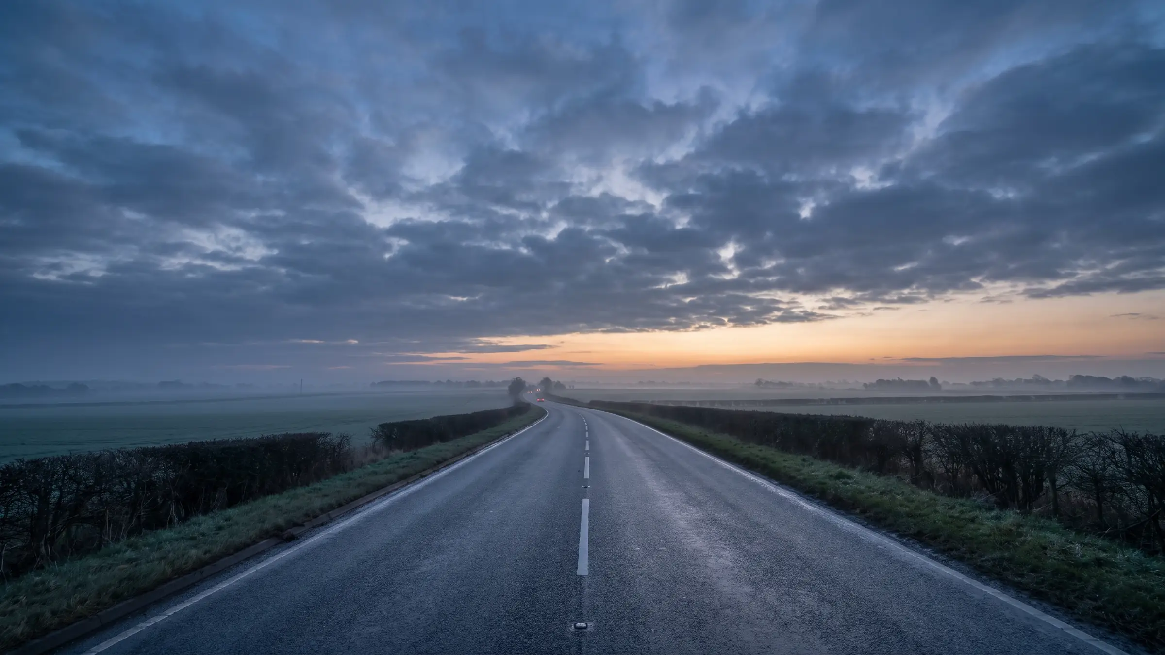 An open Lincolnshire A-road heading toward a dawn horizon, mist over the fields